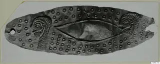 Elongated oval metal object with embossed dots and eye-like motifs at each end