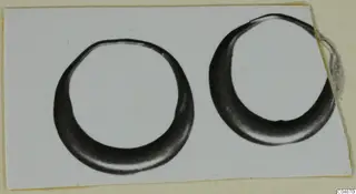 Two dark, hoop-shaped rings photographed side by side on a white card mount.