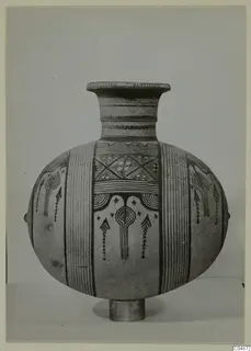 Pottery Bichrome IV jug with a flaring neck, painted vertical bands and a central motif, shown on a short stand.