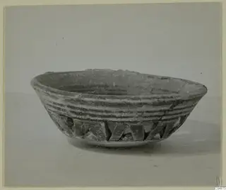 Shallow pottery bowl with grooved sides and a band of angular notches on the lower wall, shown on a plain surface