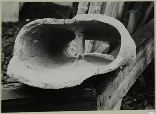 Terracotta object with a hollow interior divided by a central upright stem, resting on a wooden board