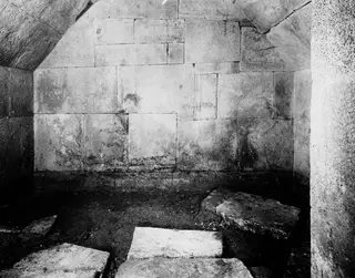 Interior of Tomb 2 at Amathus, showing large stone block walls, a sloping stone ceiling and fallen slabs on the floor.