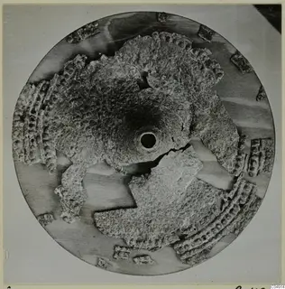 Corroded bronze weapon fragments arranged around a central funnel-shaped piece with a round opening, seen from above