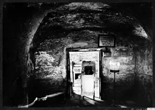 Interior of the Panagia Faneromeni tomb at Kition, a vaulted chamber with a doorway, a draped table and a candle stand