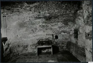 Interior of a built tomb chamber with a small wooden table and a hanging lantern on chains