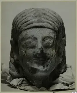 Limestone head from Kition, with ridged hair, photographed on folded cloth against a grey background.