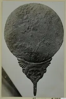 Round plate above a face-shaped figure with a long stem, from Marion
