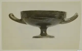 Footed black-surfaced bowl with two horizontal handles, shown in side view against a pale background.