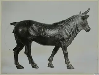Bronze statuette of a standing bull, shown in side view facing right against a pale grey backdrop