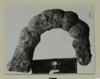 Corroded bronze personal adornment from Amathus, shaped as an open arch, photographed on a card mount