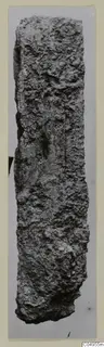 Corroded iron object from Amathus, long and narrow with a crusted, pitted surface, shown upright against a pale card