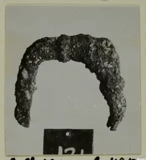 Corroded bronze arch-shaped object from Amathus tomb 2-26, with a number label in front