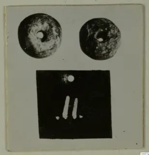 Photo mount with two round perforated objects above a dark photograph of a small object with a hole and two pale bars