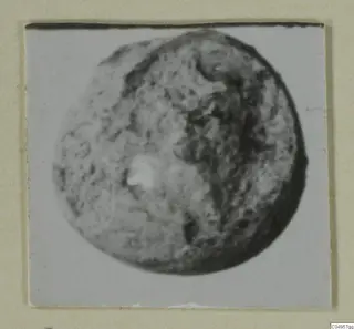 Close view of a rounded, pitted find, possibly a bead, on a mounted photograph