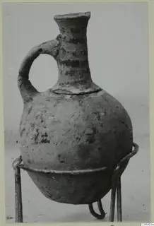One-handled jug from Milia with dark painted bands, standing on a metal wire stand