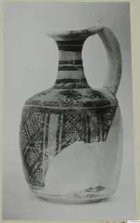 Painted jug with a loop handle and a broad band of geometric patterns on the body, photographed against a plain background.
