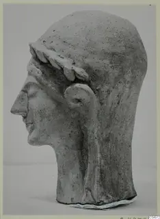 Terracotta head of a figure in profile facing left, wearing a leaf wreath, shown against a pale background