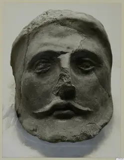 Face with a moustache from Mersinaki, grey-brown and cracked, shown frontally on a pale background