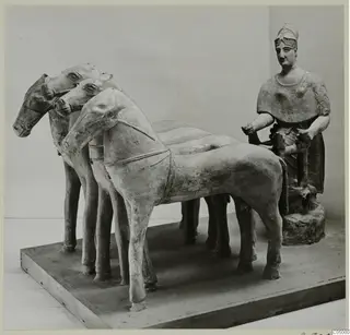 Terracotta group of horses harnessed in a row, with a seated figure in a helmet at the right, on a wooden plinth