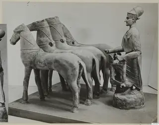 Terracotta group of a figure at a chariot rail behind a team of four horses on a flat plinth
