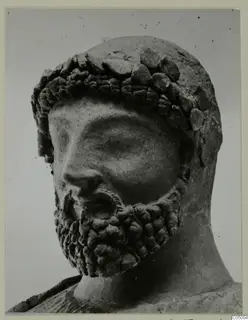 Close photograph of a bearded male head sculpture with a band of rounded forms across the hair and forehead.