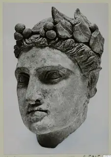 Stone head of a statue from Mersinaki, wearing a wreath of leaves and round berries in its hair.