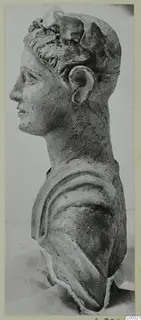 Bust of a figure in profile facing left, with curled hair, a raised headdress and drapery over the shoulder