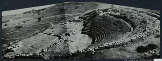 The theatre at Soli: curved rows of stone seating on a slope, with low stone walls and fields and trees beyond.