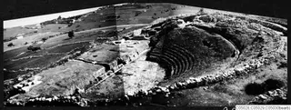 The theatre at Soli: curved rows of stone seating cut into a slope, with walls and cultivated fields beyond.