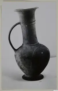 Pottery Base-Ring Ware jug with a single strap handle and flaring rim, shown standing on a pale surface