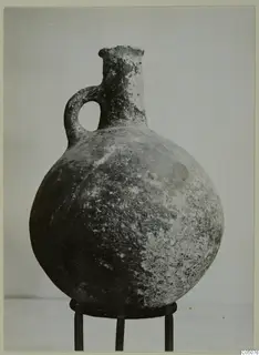 Red Polished III jug from Lapithos with a single loop handle, standing on a metal stand