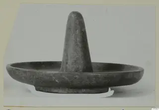 Dark grey stone bowl with a tall tapering post rising from the centre, photographed on a light background