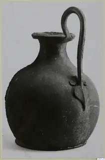 Bronze pot with a single arched handle and a flat, flaring rim, shown against a pale background