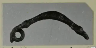 Curved, dark corroded metal object with a small round loop at one end, from the Kastros tombs at Lapithos