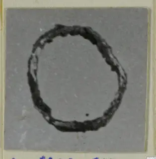 Bronze loop, a dark ring-shaped metal object, photographed on a grey card.