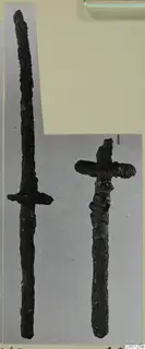 Two corroded iron weapons from Lapithos Kastros tombs, one long and one short, on a grey backdrop.