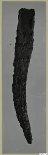 Corroded iron knife, curved and tapering to a point, photographed against a grey backdrop.