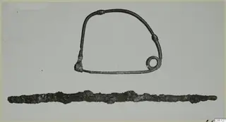 Two iron objects on a pale ground: a bow-shaped wire with a coiled end and a long, corroded iron bar below.