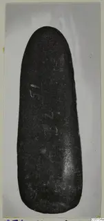 Axe head from Petra tou Limniti, a dark smooth stone object photographed on a grey background