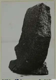 Dark stone fragment from Petra tou Limniti, photographed upright against a plain background.