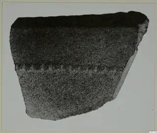 Fragment of a dark grey stone vessel wall with a pale band of tool marks across the middle