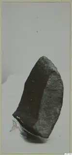 Dark stone fragment from Petra tou Limniti, photographed on a pale background