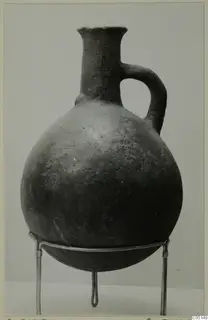 Red Polished III jug with a tall neck and single loop handle, standing on a wire stand