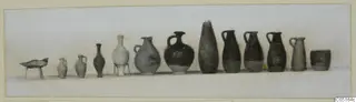 Row of pottery vessels from Kountoura Trachonia Tomb 12: jugs, juglets, a dish on legs and a cup, set in a line.