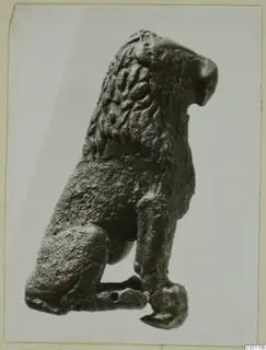 Bronze figure of a seated animal with a ridged mane, shown in side view.