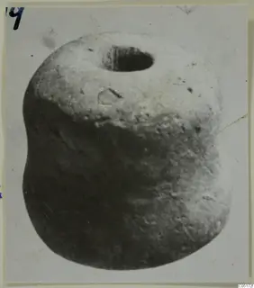 Close photograph of a squat, rounded small find with a wide hole in its top, mounted on a card