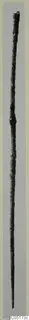 Long, thin corroded bronze tool photographed upright against a grey background