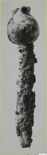 Heavily corroded iron object with a rounded head and a long, pitted shaft, photographed upright.