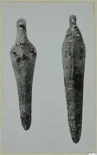 Two corroded bronze knives side by side against a pale background, one with a handwritten number label