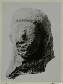 Terracotta head fragment with a smooth domed top, worn face and broken lower edge